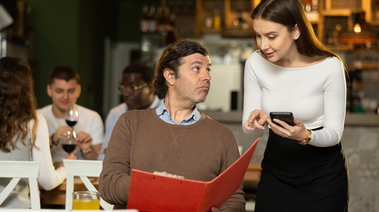 Customer holding restaurant menu with server pointing at it