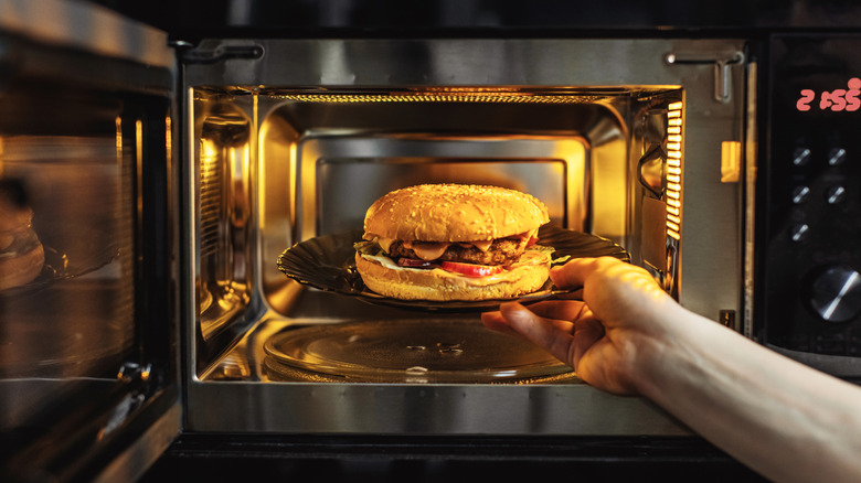 Hand holding plate of burger inside opened microwave