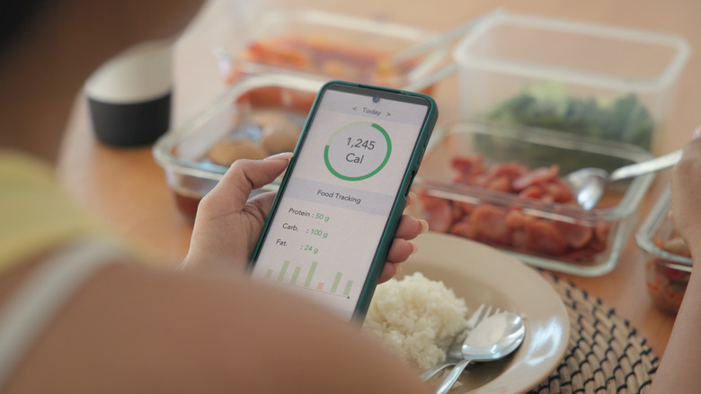 Person looking at calorie-counting app with prepped meals in background.