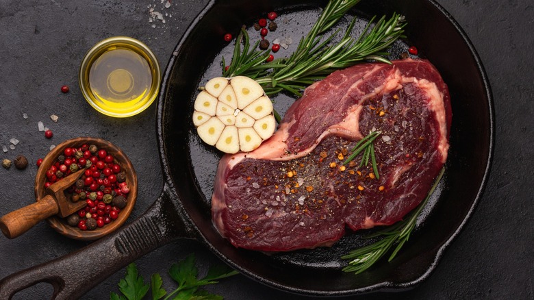 Raw steak in pan with garlic, herbs, and seasonings