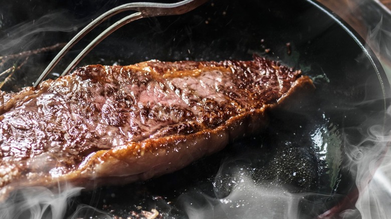 Person cooking steak in smoking pan