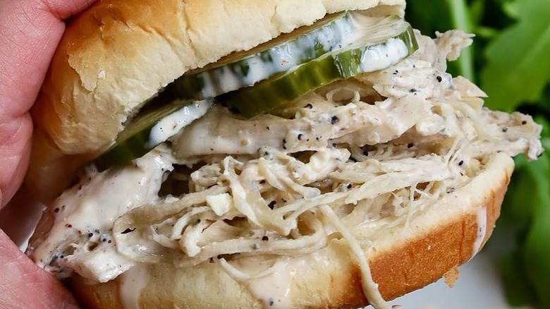 hand holding chicken and alabama white sauce sandwich