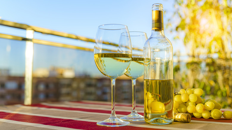 Two glasses of sauvignon blanc with opened bottle on an outdoor patio table.