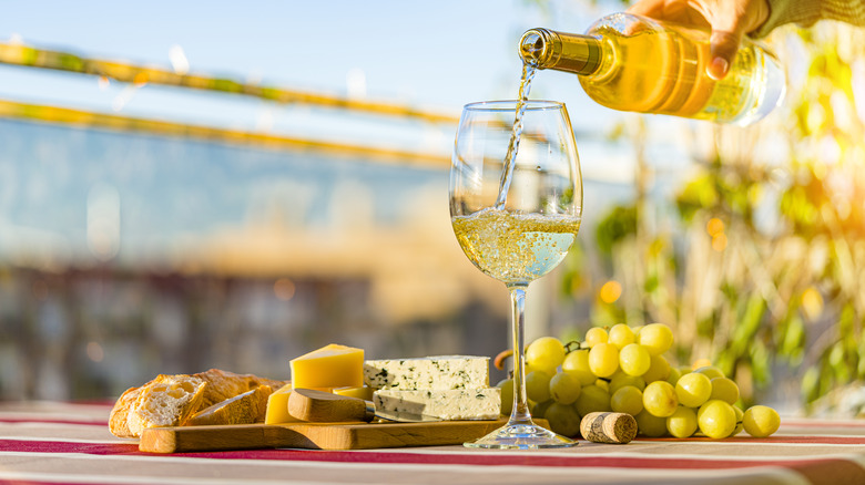 White wine being poured into a glass with grapes and cheese