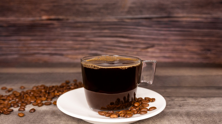 A long black coffee made in a clear cup, surrounded by coffee beans