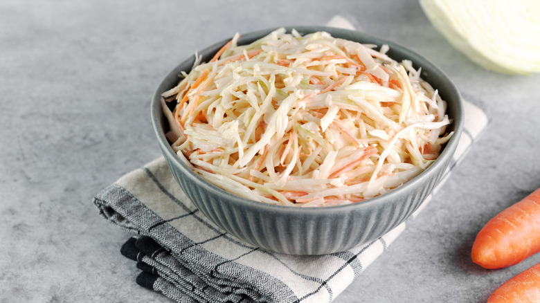 Coleslaw in a ceramic bowl on top of a cloth napkin