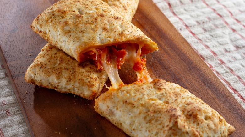 Two Hot Pockets on a wooden board, one split in half resting on top of another