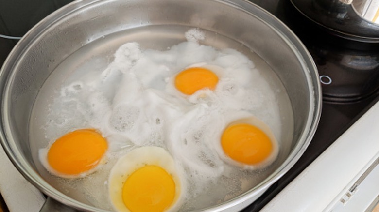 Eggs poaching in a pot of water on a stovetop