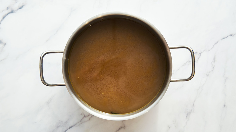 Beef broth in a metal cooking pot on a marble countertop