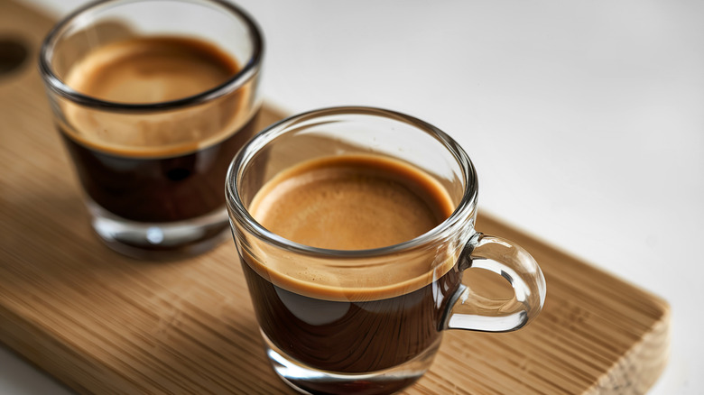 Two shots of espresso in small glass cups on a wooden board.