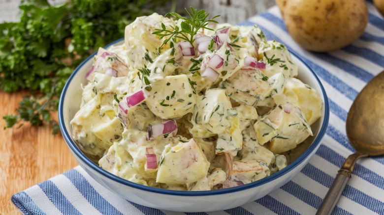 A bowl of potato salad with herbs and diced red onion