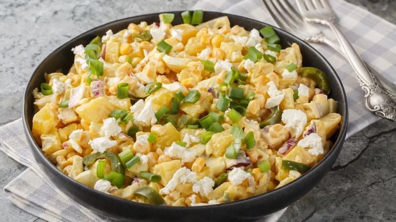 A bowl of Mexican-inspired potato salad with sweetcorn, jalapeños, and cheese topped with spring onion