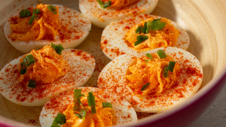 A closeup of deviled eggs topped with green onions and lots of paprika