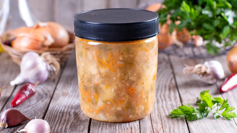 Soup in lidded jar on a wood table with vegetables and herbs