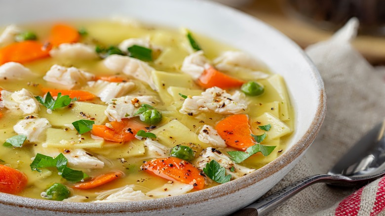 A bowl of chicken noodle soup with carrots and fresh herbs