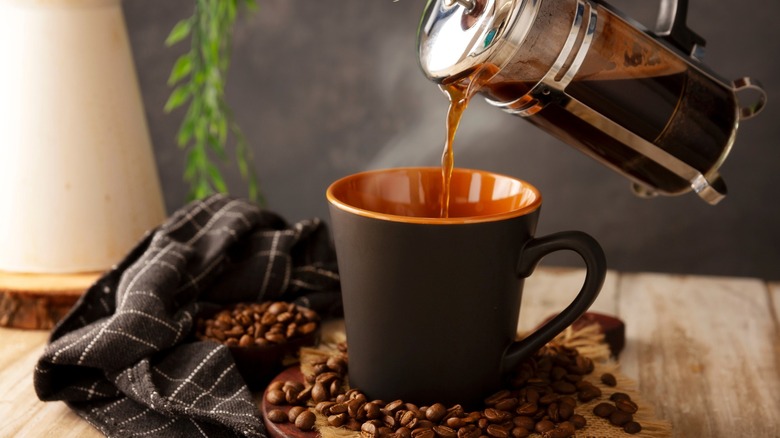 Person pouring coffee into black cup from French press