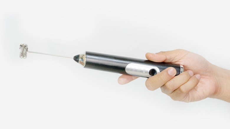 A hand holding a milk frother against a white background