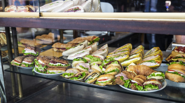 A deli display of assorted sandwiches on trays in a glass case