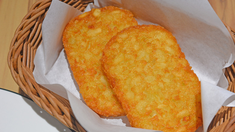 A closeup of golden-brown hash browns on paper in a wicker basket