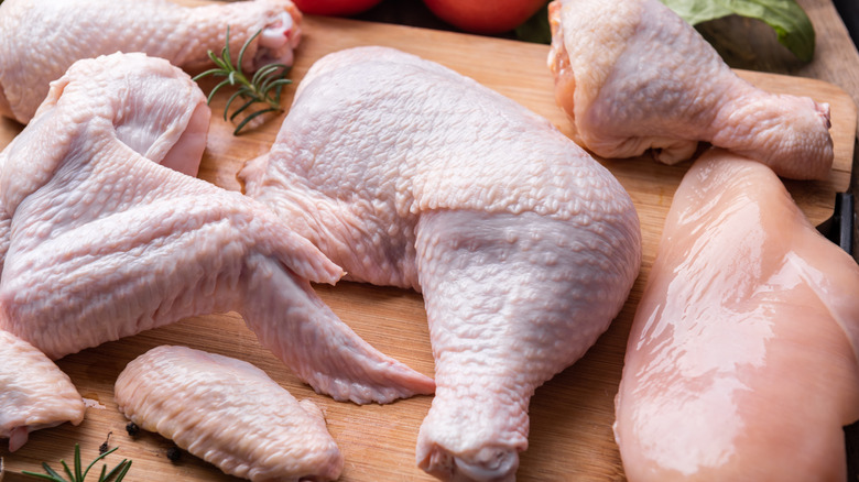 Raw chicken wings, drumsticks, and breast on a wooden board