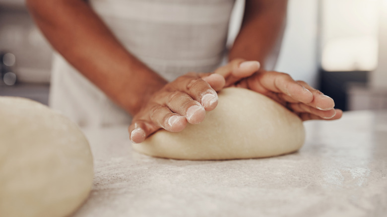 A person kneading a mound of pizza dough on a kitchen counter