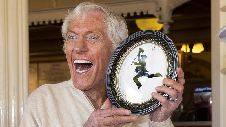 Dick Van Dyke holding up a framed image of a dancing chimney sweep, smiling widely