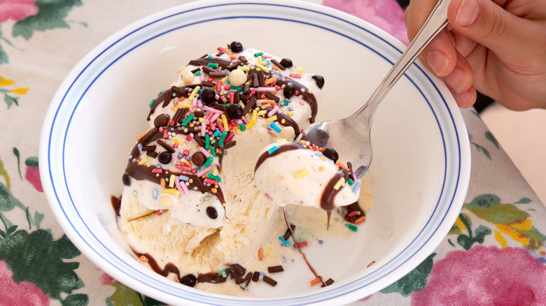 A closeup of vanilla ice cream in a bowl topped with chocolate syrup, sprinkles, and chocolate chips
