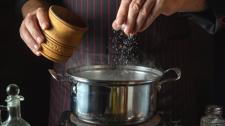 A chef adds salt to a pot of soup