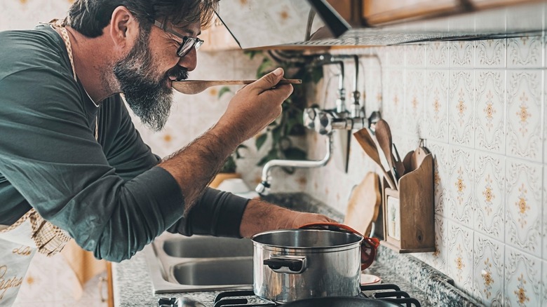 A man tastes something from a pot with a wooden spoon