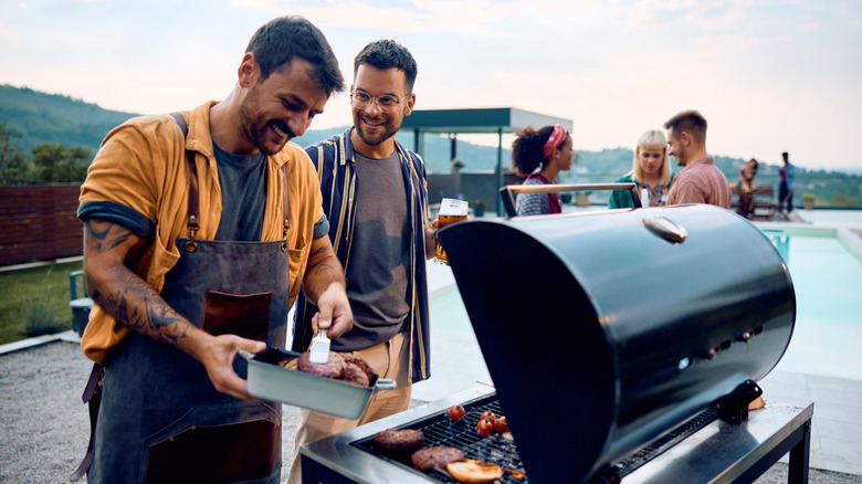 Some friends grilling hamburgers on the grill outside by a pool