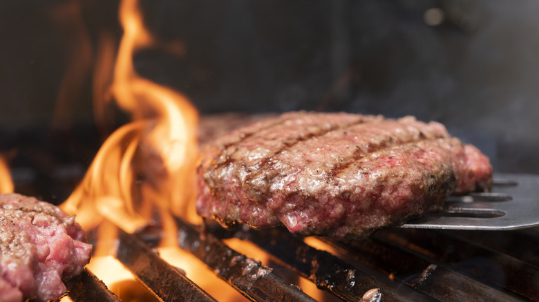 A hamburger patty being lifted off a flaming grill with a metal spatula.