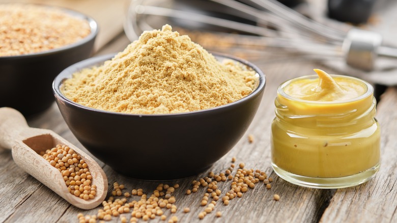 Mustard seeds in scoop, a bowl of dry mustard, and a jar of prepared mustard