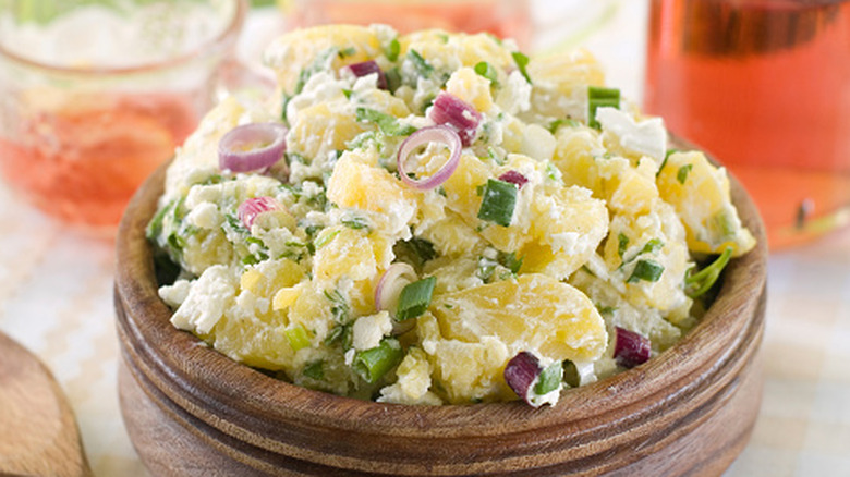 Potato salad with onions in a wooden bowl near some iced tea.