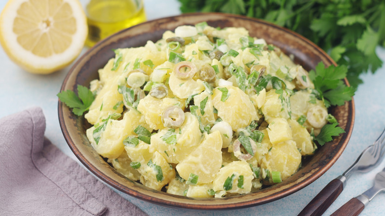 Bowl of potato salad surrounded by lemon, cilantro, and silverware.