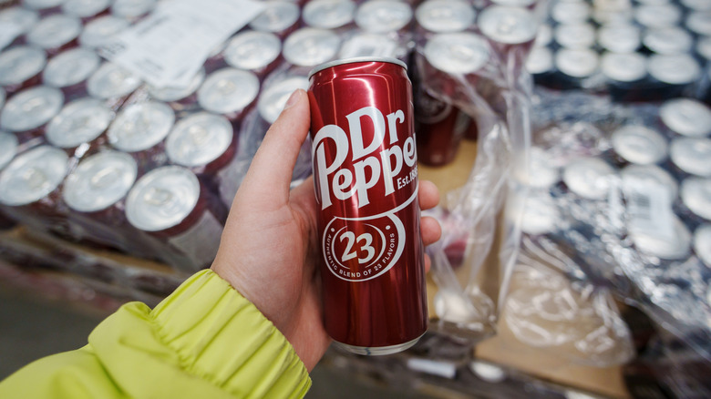 Someone holding can of Dr Pepper in front of crates of cans