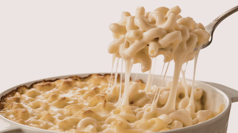 A dish of creamy mac and cheese with a forkful and cheese pull