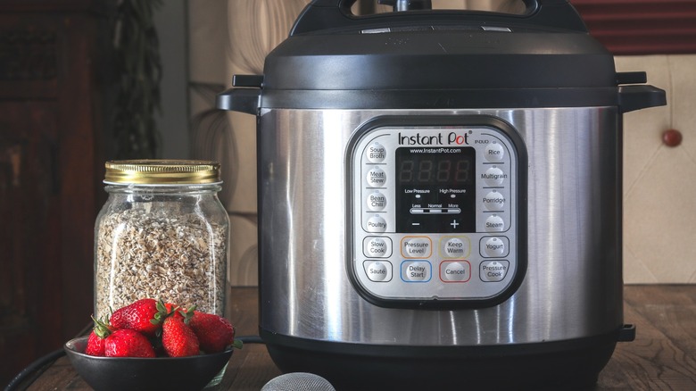 A jar of rolled oats and a bowl of fresh strawberries beside an Instant Pot