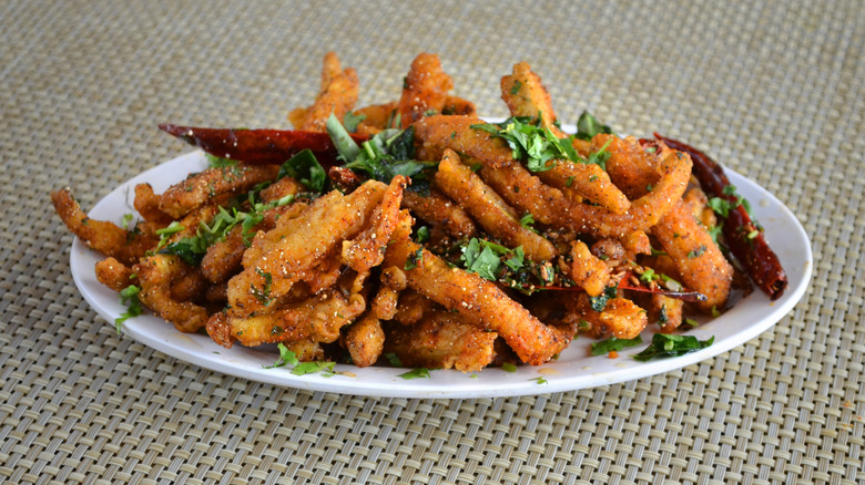 A plate of seasoned baby corn fritters with parsley garnish and dried red peppers