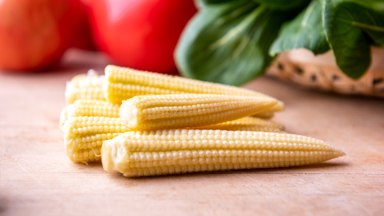 A small pile of baby corn with vegetables in the background