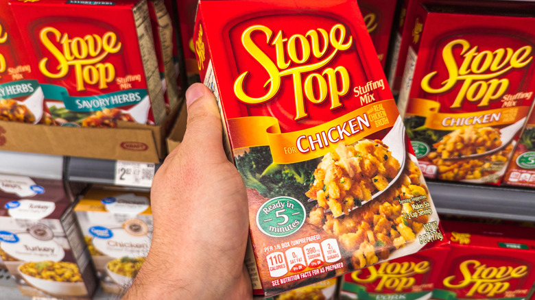 A hand holding a box of chicken Stove Top stuffing in a grocery aisle