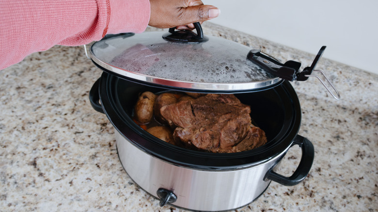 High angle view of a woman's hand checking on food in slow cooker.