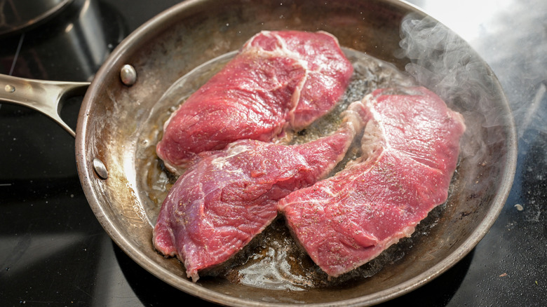 Three cuts of meat brown in a pan
