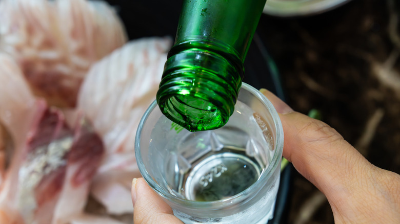 Hands pouring a green-bottled soju into a shot glass