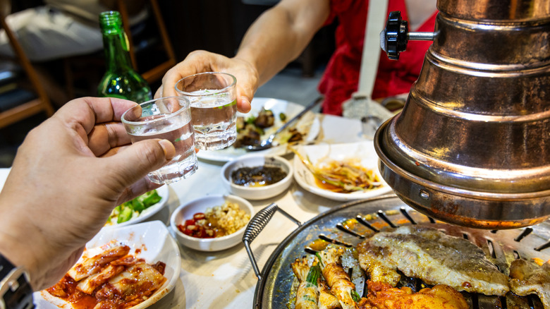 Two hands cheering with soju with an array of food around them