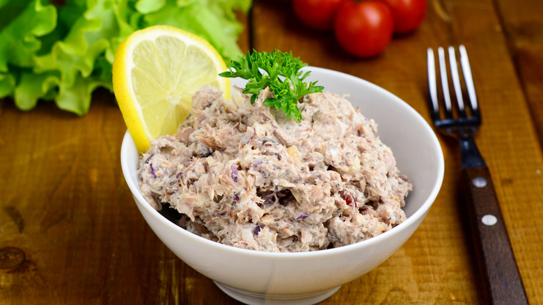 A creamy bowl of tuna salad with a lemon slice alongside it