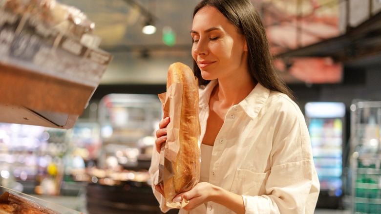 A woman smells a loaf of bread in a grocery store