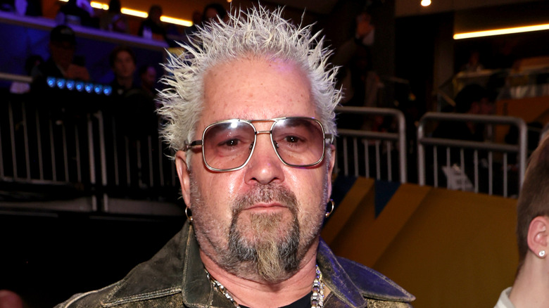 Guy Fieri wearing sunglasses and a worn leather jacket at an indoor event