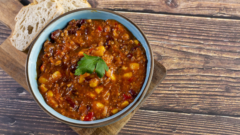 A bowl of chili with corn and beans, garnished with cilantro and served with bread