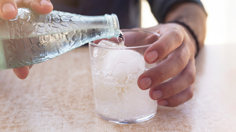 Hands pouring bottle of sparkling water over ice in a glass