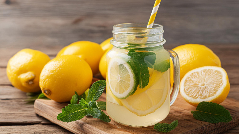 Lemons and a lemon refresher drink in a mason jar mug with a straw